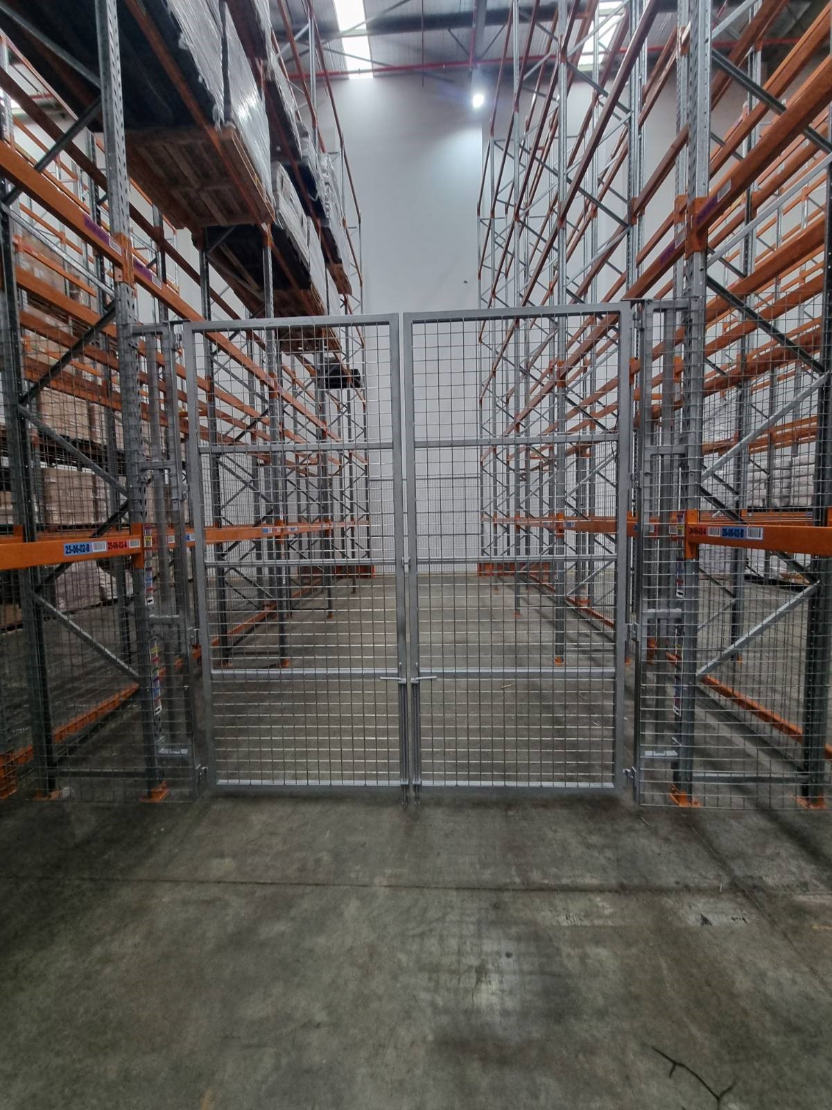 Custom fabricated steel security gate in a warehouse filled with pallet racking.