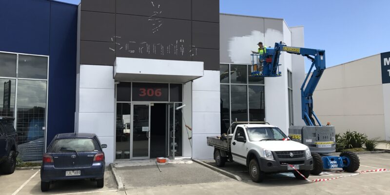 The exterior of a retail building having a defit done; the building has been stripped of branding and is being painted white.
